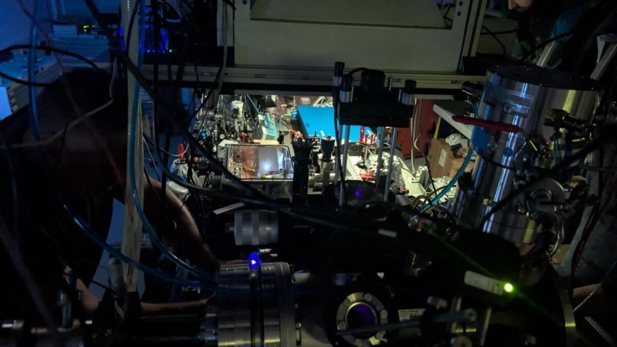 Darkened laser laboratory at TU Wien with the vacuum chamber that holds the thorium-doped crystal in the foreground and a researcher adjusting the laser at top right